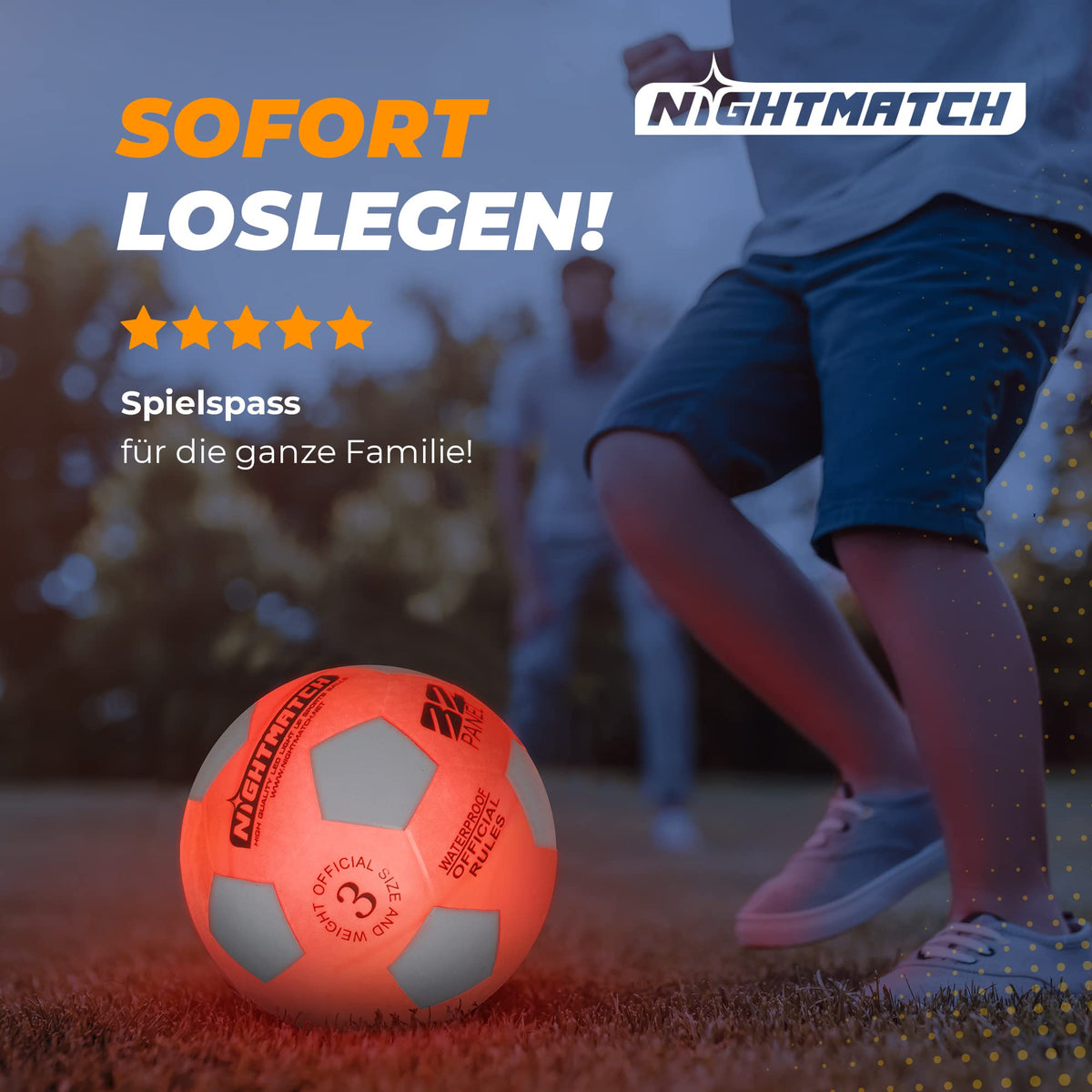 Leuchtfußball - Komplettset - Weiss-Orange - Gr.3 leuchtet auf dem Spielfeld bei Dämmerung, Spieler im Hintergrund in Bewegung.