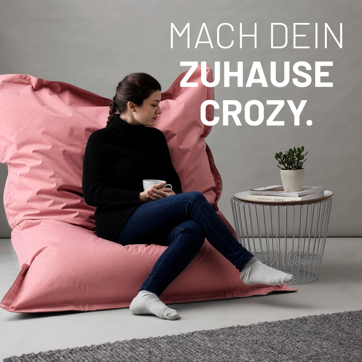 Sitzsack Classic XXL (380 L) - indoor & outdoor - Pastell Pink mit entspannter Frau in bequemer Sitzposition neben modernem Beistelltisch und Pflanze.