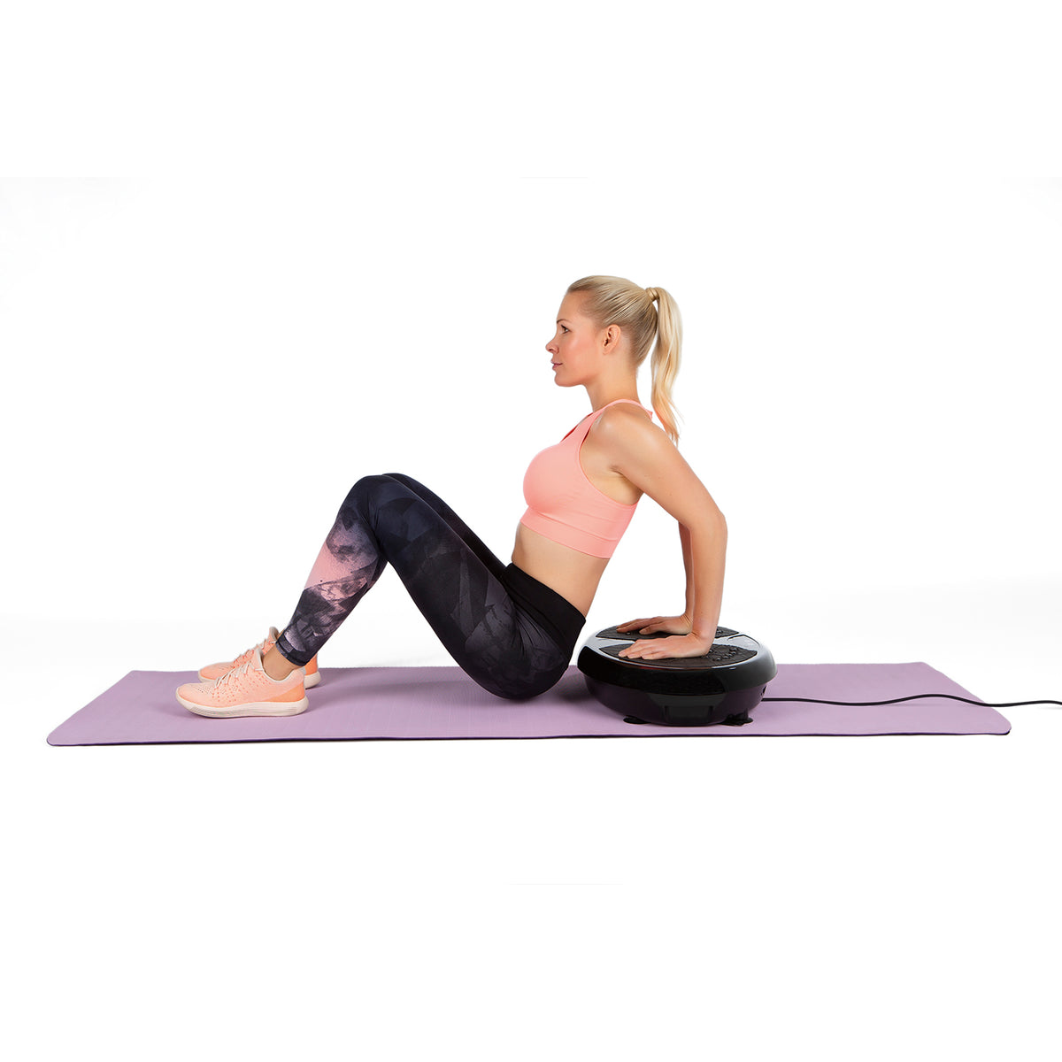 Frau trainiert mit Vibrationstrainer auf Yogamatte für Ganzkörpertraining mit Expanderbändern und LED-Display