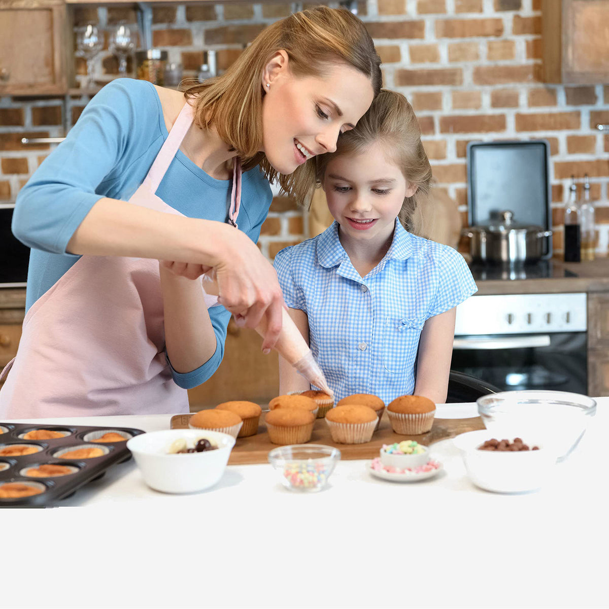 Einwegspritzbeutel-Set - 100 Stck., Mutter und Tochter verzieren Muffins gemeinsam in der Küche mit Spritzbeutel.