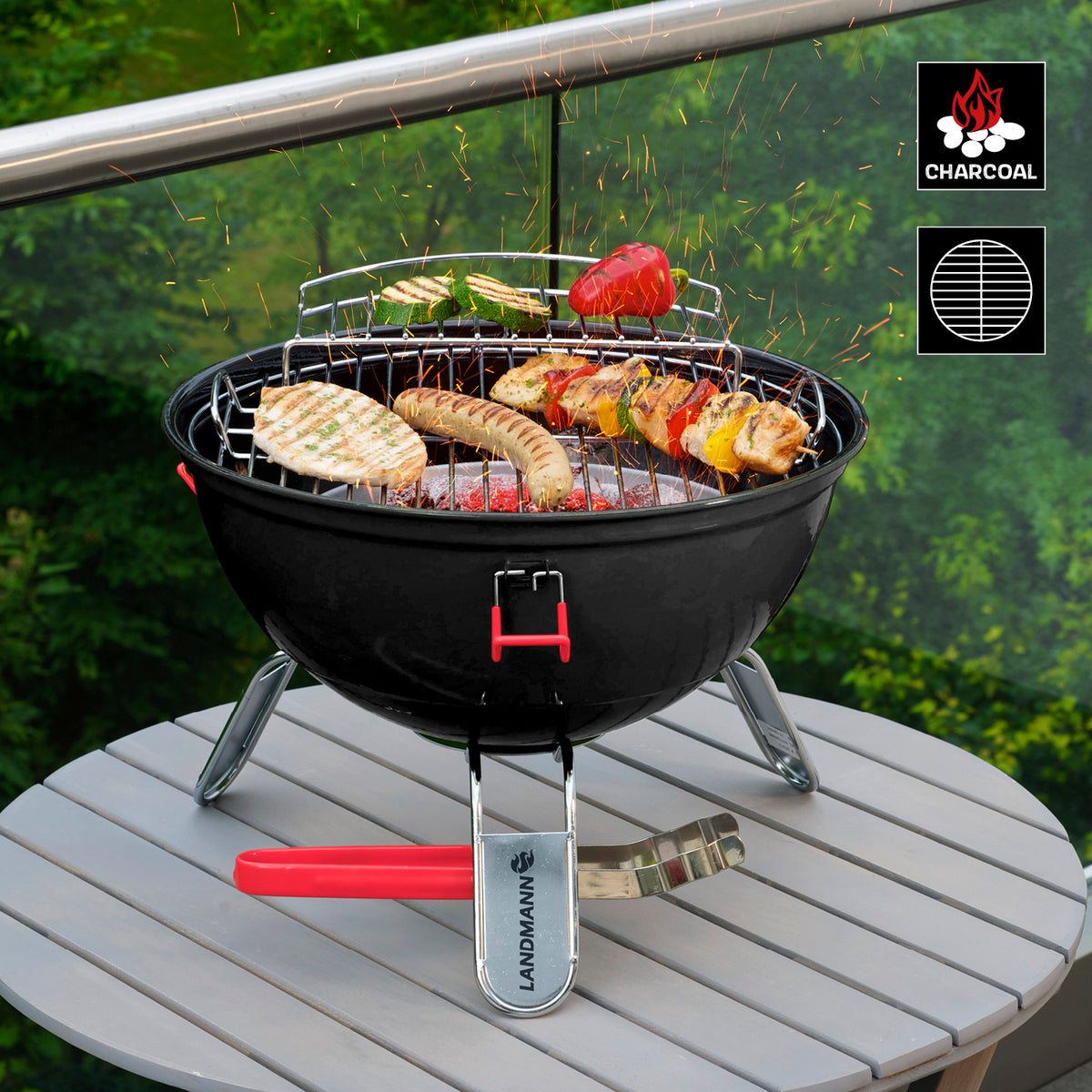 Piccolino King Holzkohlegrill mit pulverbeschichtetem Deckel, gummierten Klammern und Edelstahl-Grillzange auf Tisch im Garten.