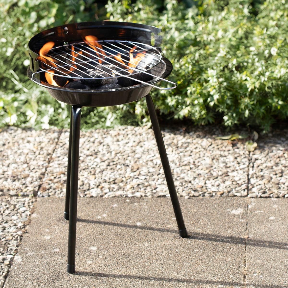 Holzkohle-Rundgrill mit verchromtem Grillrost, drei Beinen und Flammen, ideal für mobiles Grillen im Garten oder Park.