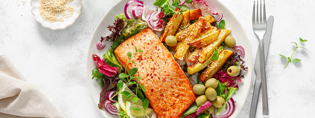 Ein Teller mit Lachs, Kartoffel-Spalten und Salat, daneben Besteck.