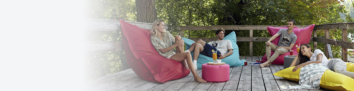 Eine Gruppe Männer und Frauen liegen und sitzen auf LUMALAND XXL Sitzsäcken für den Outdoor-Bereich auf einer Terrasse. 