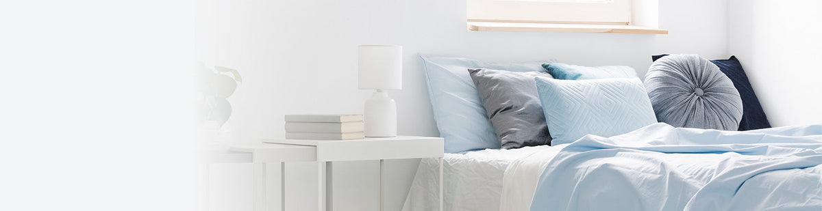Ein Bett mit diversen hellblauen und grauen Kissen, daneben ein weißer Nachttisch.