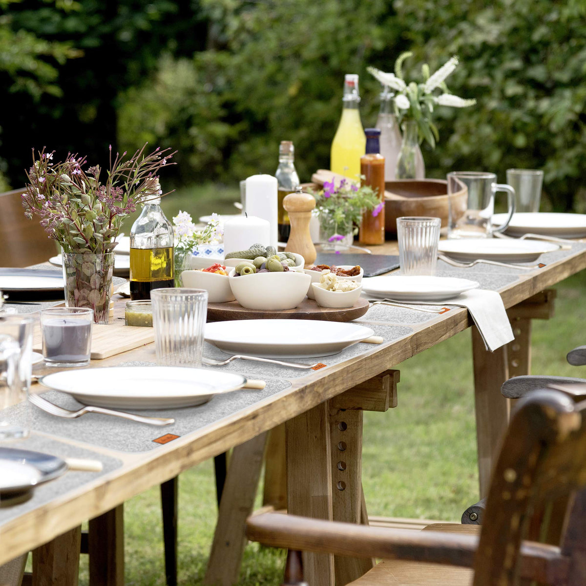 Filz Tischset - 12-teilig inkl. Glasuntersetzer - Hellgrau mit sommerlich gedecktem Gartentisch, frischen Kräutern und schlichten weißen Tellern.