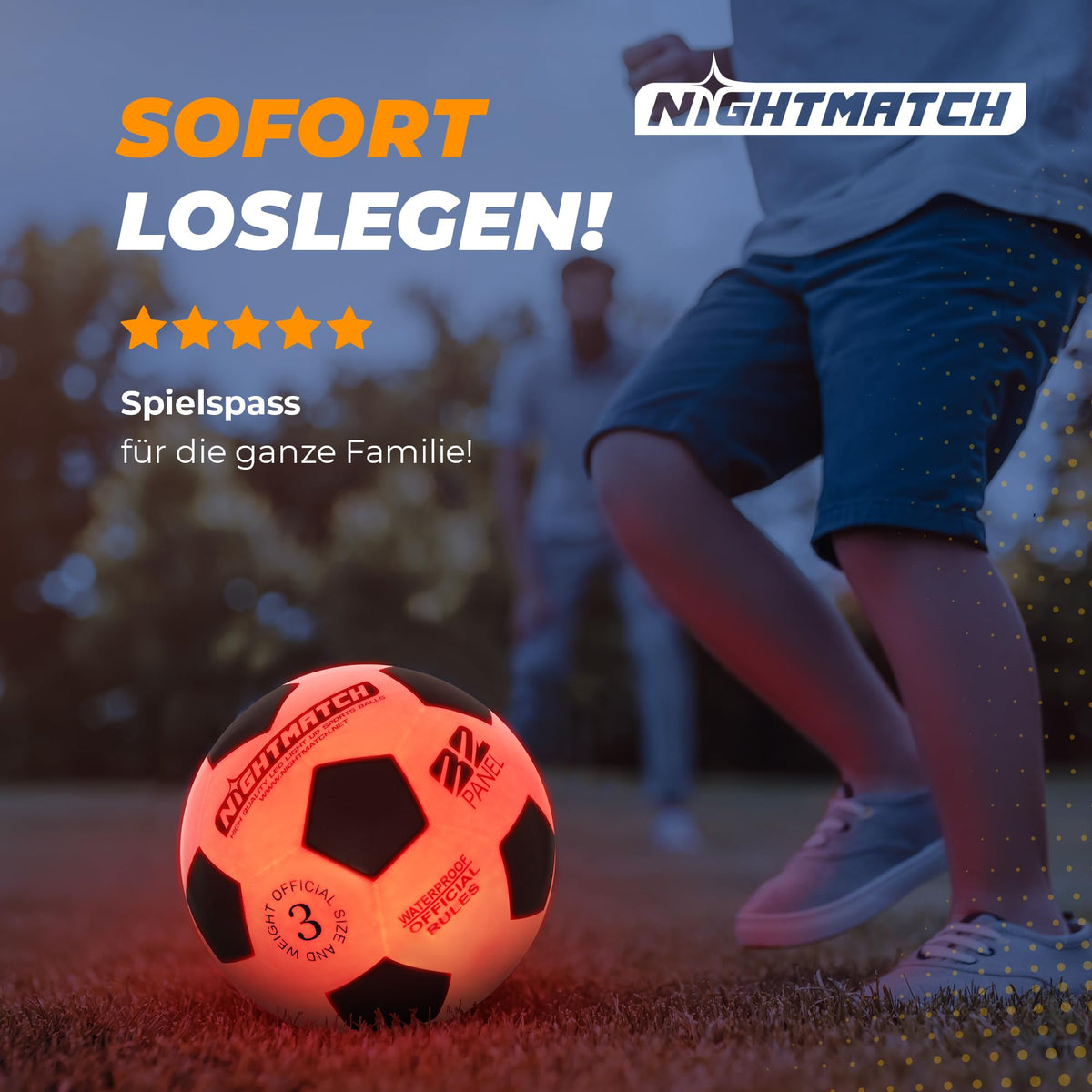 Leuchtfußball - Komplettset - Schwarz-Orange - Gr.3 auf Rasen, leuchtend beim Spielen im Freien am Abend mit aktiven Spielern im Hintergrund.