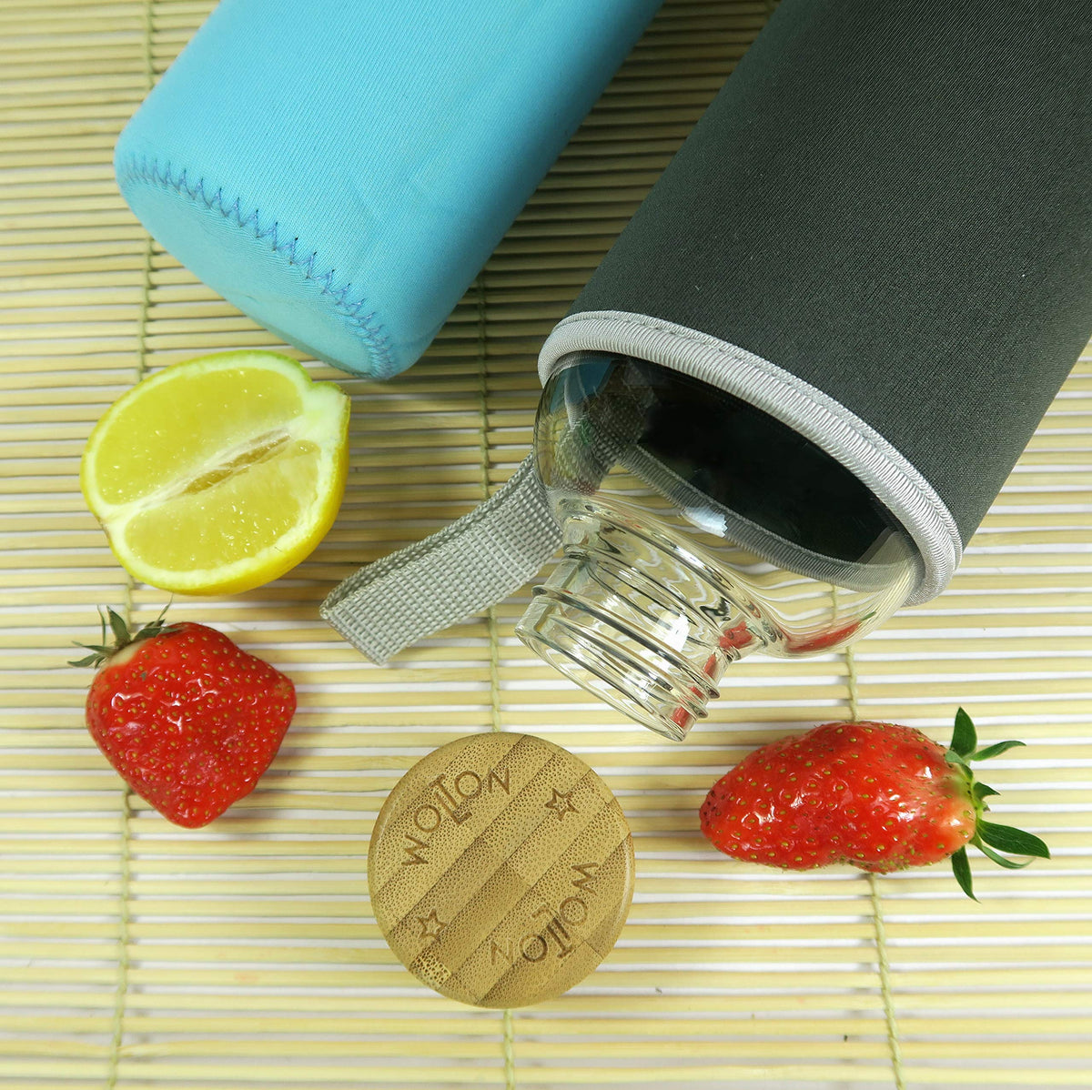 Trinkflasche mit Bambusdeckel - 550 ml - Grau mit grauem Schutzbezug, aufgelegt neben frischen Erdbeeren und einer Zitronenhälfte.
