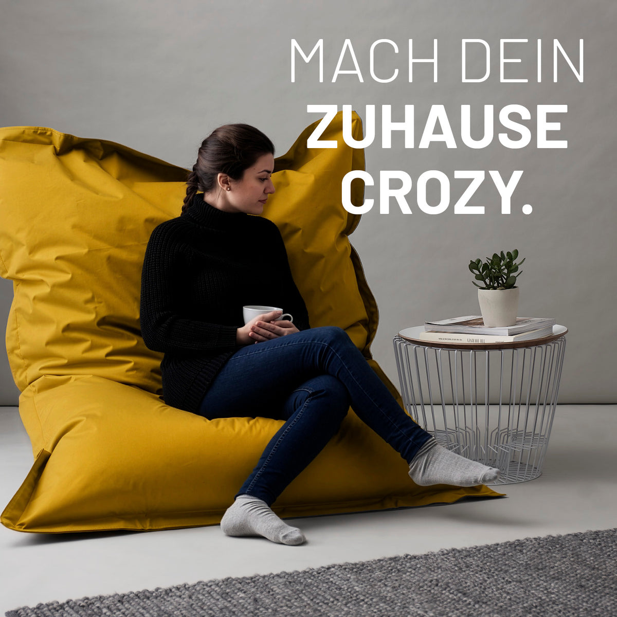 Sitzsack Classic XXL (380 L) - indoor & outdoor - Senfgelb mit Frau in entspannter Sitzhaltung vor neutralem Hintergrund und kleinem Beistelltisch