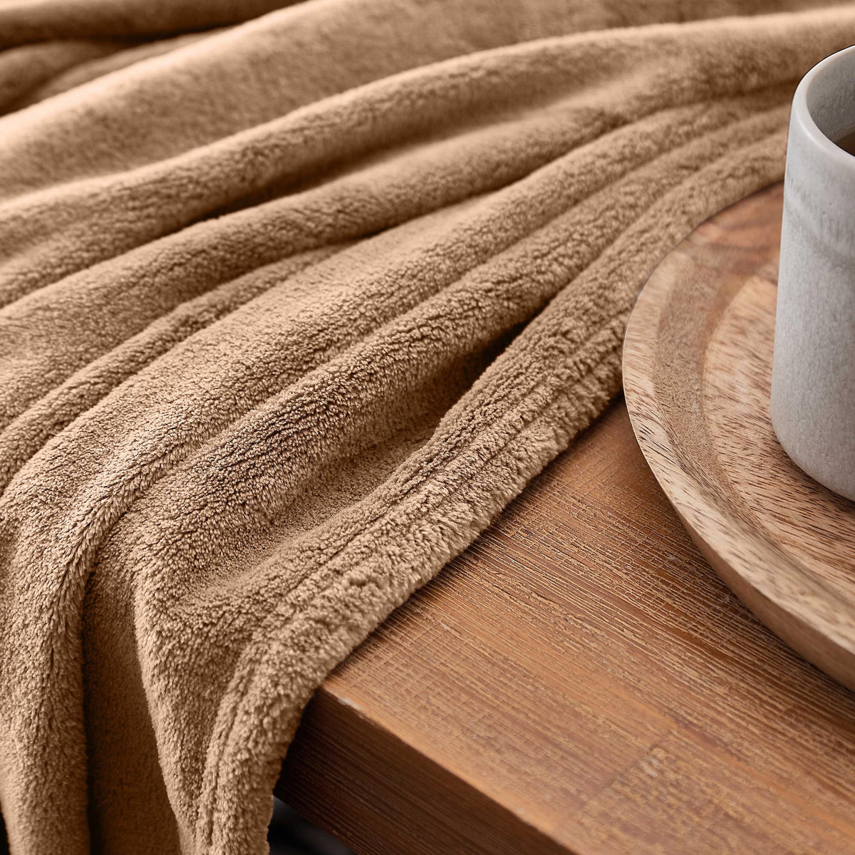 Kuscheldecke - 220x240 cm - Sofadecke & Tagesdecke - Hellbraun aus weichem Coral-Fleece auf Holztisch mit Kaffee.