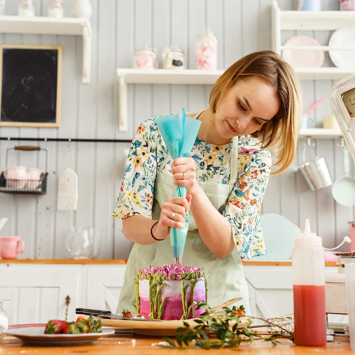 Frau verziert mit Spritztüllen-Set - 38-teilig Torte in heller Küche, benutzt blaue Spritzbeutel für kreative Tortendekoration.