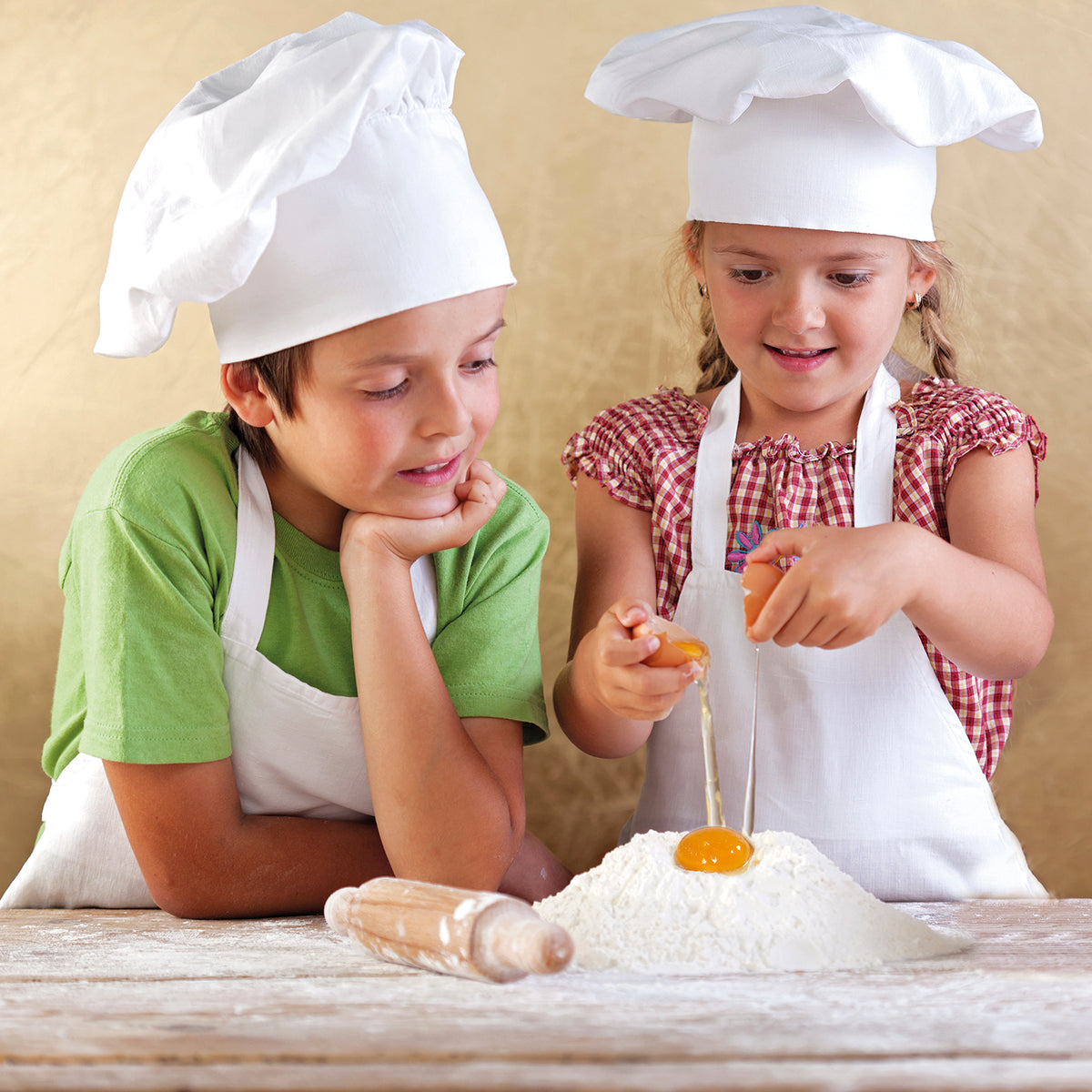Zwei Kinder mit Kochmützen backen gemeinsam mit dem Rezeptbuch inkl. Messbecher-Set - Band 1 - Für die Backprofis von morgen.