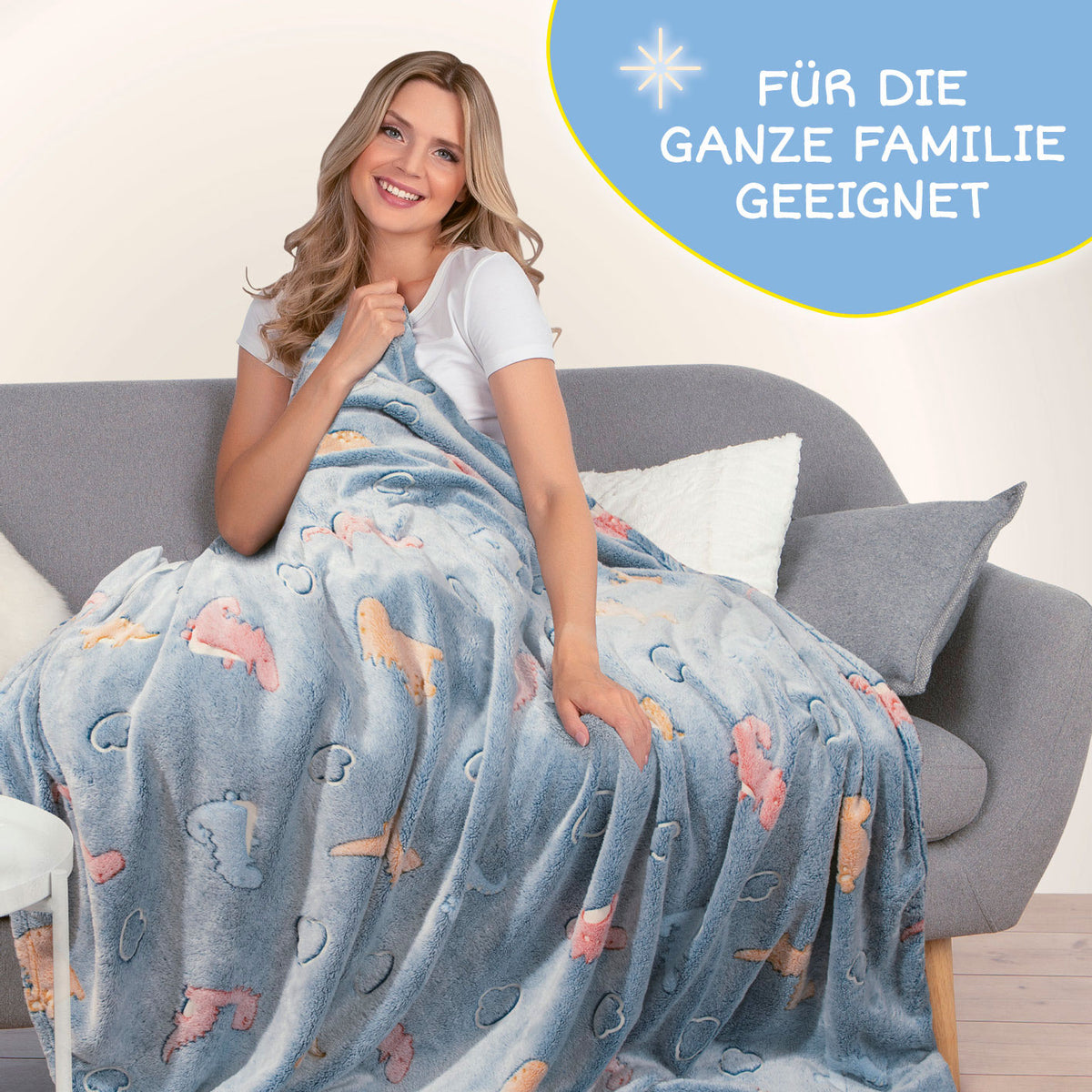 Frau auf Sofa mit Verwandlungskissen Glow in the dark - Kuschelkissen & Kuscheldecke - Dino aus weichem Flanell-Fleece