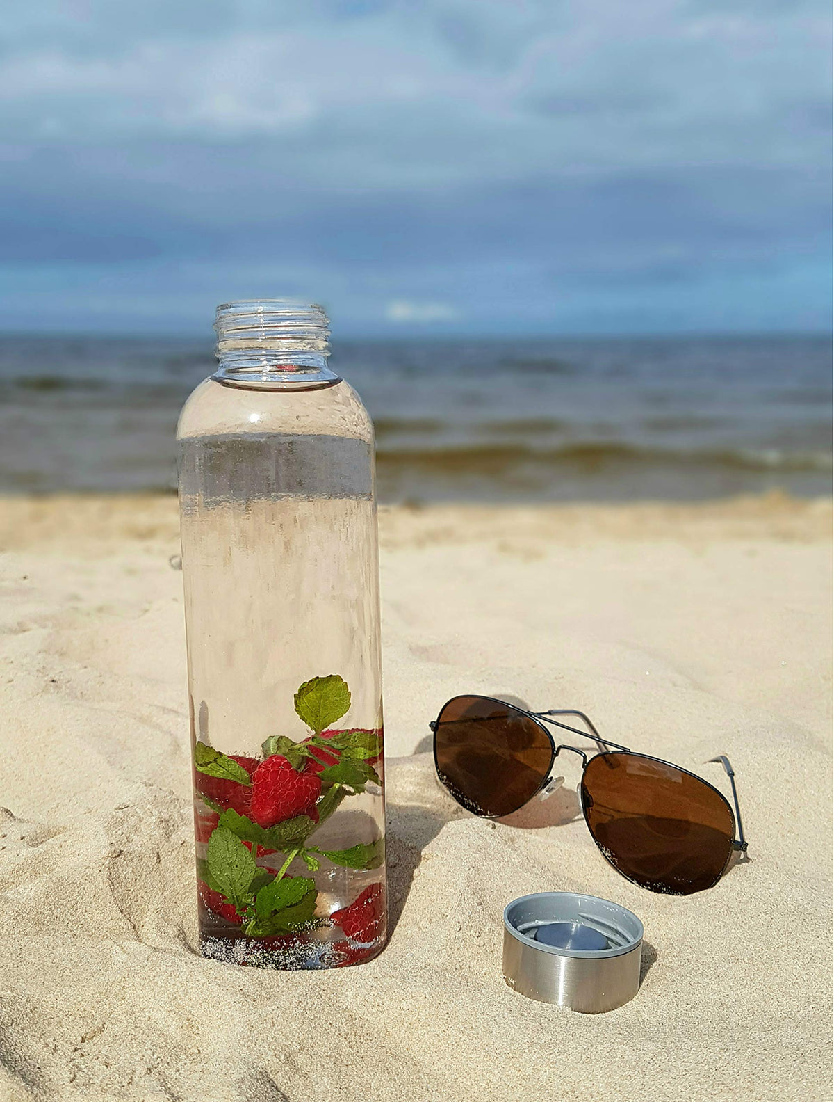 Glasflaschen-Set - 6 Stück à 500 ml, robuste und stilvolle Kalk-Natron-Glasflasche am Strand mit Früchten und abgenommenem Deckel.