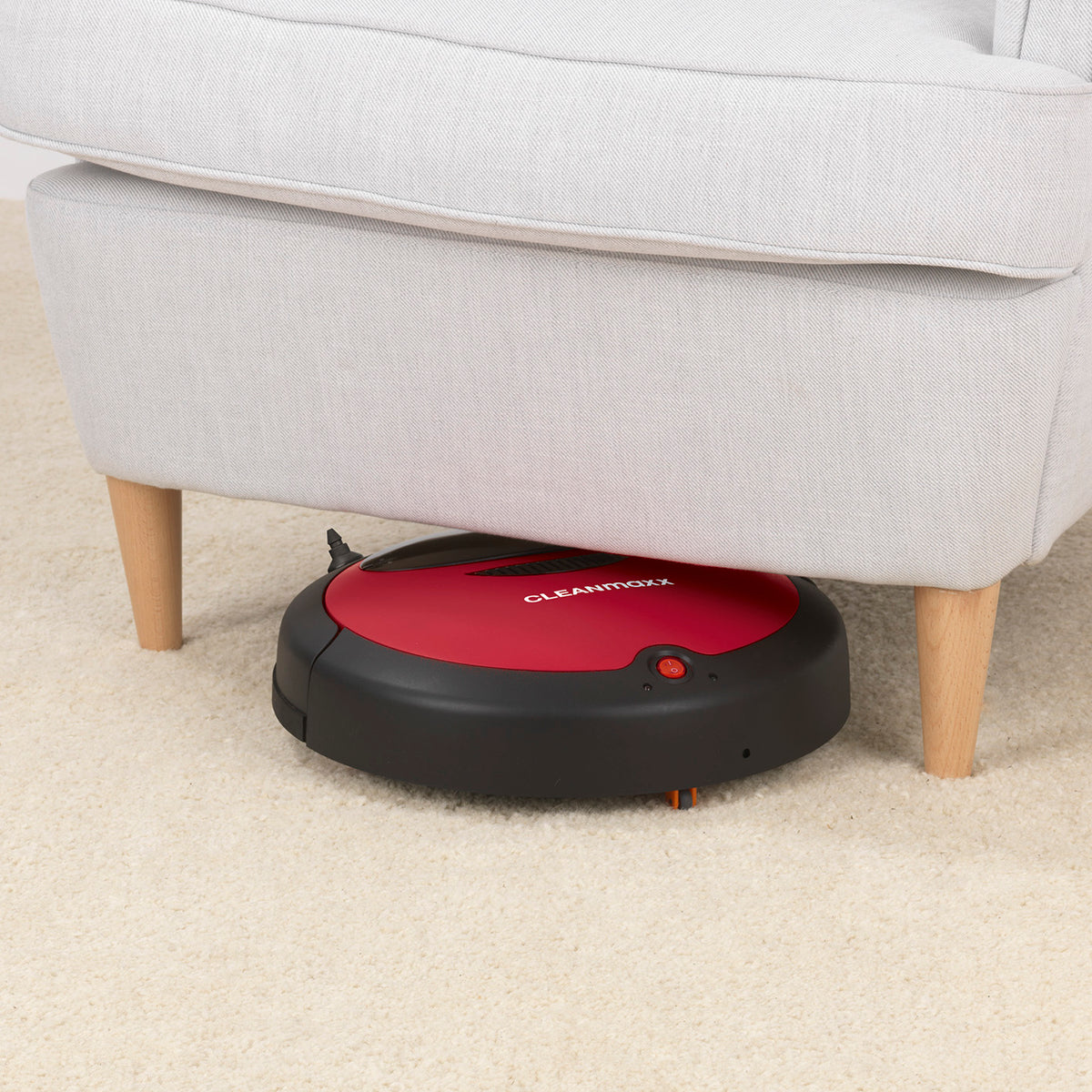 Saugroboter 2in1 - rot/schwarz reinigt Teppichboden unter einem hellen Sofa mit sensorgesteuerter Navigation.
