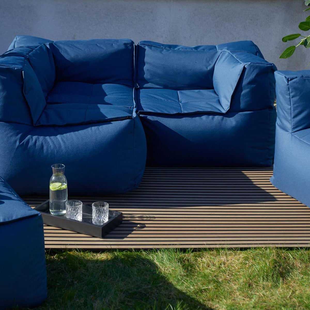 Moderne LUMALAND Outdoor-Lounge mit blauen Polstersesseln auf Holzdeck und Tablett mit Karaffe und Gläsern auf grünem Rasen.